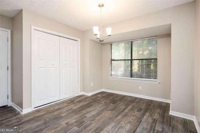 unfurnished bedroom with wood finished floors, a closet, baseboards, and a chandelier