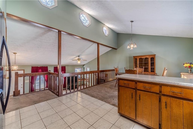 kitchen with brown cabinetry, lofted ceiling, light colored carpet, and light tile patterned floors