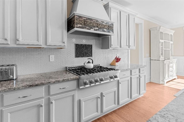 kitchen with premium range hood, decorative backsplash, stainless steel gas cooktop, light wood-type flooring, and light stone countertops