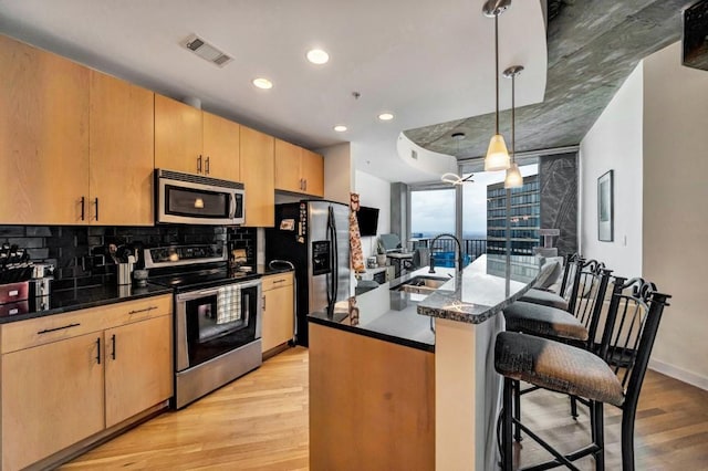 kitchen with light wood-type flooring, appliances with stainless steel finishes, sink, pendant lighting, and a kitchen bar