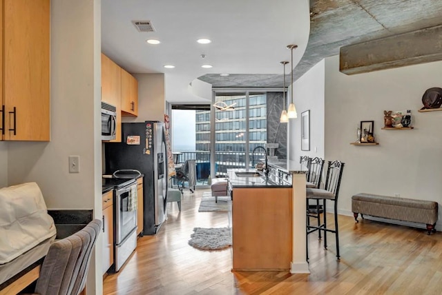 kitchen featuring stainless steel appliances, light hardwood / wood-style floors, sink, pendant lighting, and a kitchen bar