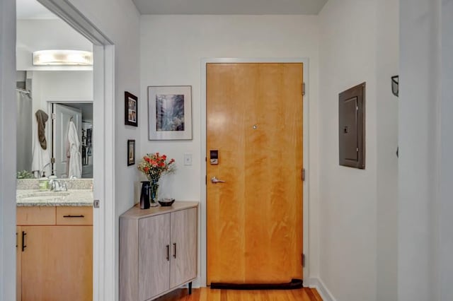 doorway to outside with electric panel, sink, and light hardwood / wood-style flooring