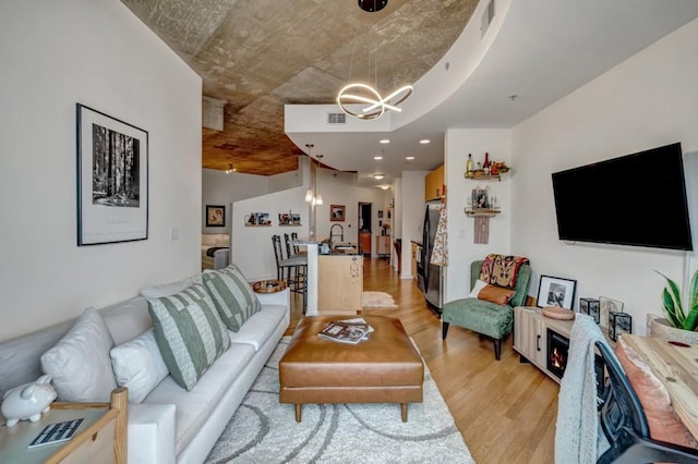 living room featuring sink, light wood-type flooring, and a chandelier