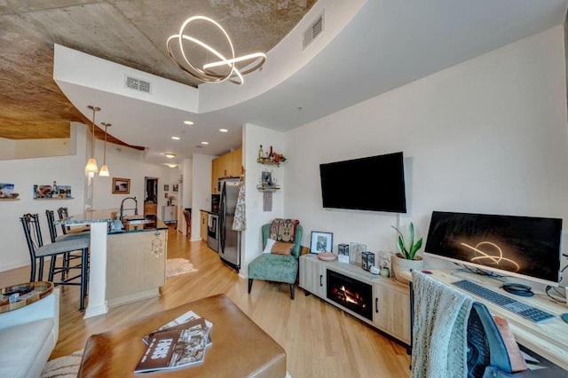 living room with light wood-type flooring, a fireplace, a chandelier, and sink