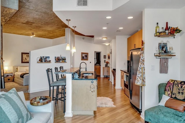 kitchen featuring hanging light fixtures, light hardwood / wood-style flooring, stainless steel refrigerator, sink, and a kitchen bar