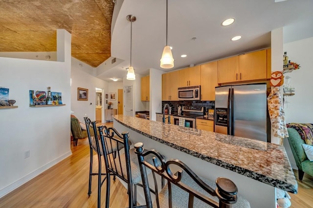 kitchen with dark stone countertops, pendant lighting, stainless steel appliances, and light wood-type flooring