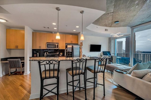 kitchen featuring appliances with stainless steel finishes, dark stone countertops, hanging light fixtures, and light hardwood / wood-style flooring