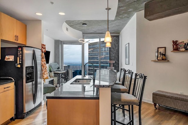 kitchen with pendant lighting, stainless steel fridge with ice dispenser, a breakfast bar, sink, and light wood-type flooring