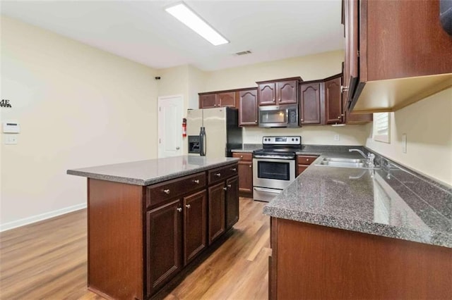 kitchen with stainless steel appliances, dark stone counters, light wood-type flooring, sink, and a center island