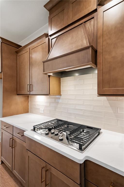 kitchen with light hardwood / wood-style floors, premium range hood, backsplash, ornamental molding, and stainless steel gas cooktop