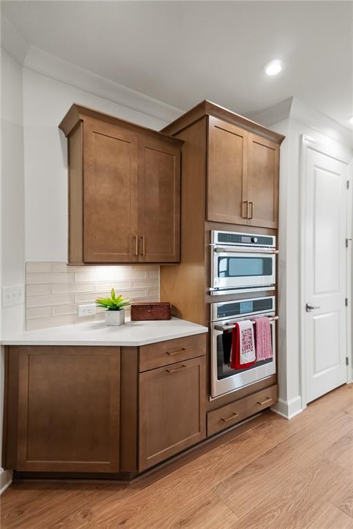 kitchen featuring crown molding, decorative backsplash, light hardwood / wood-style flooring, and stainless steel double oven