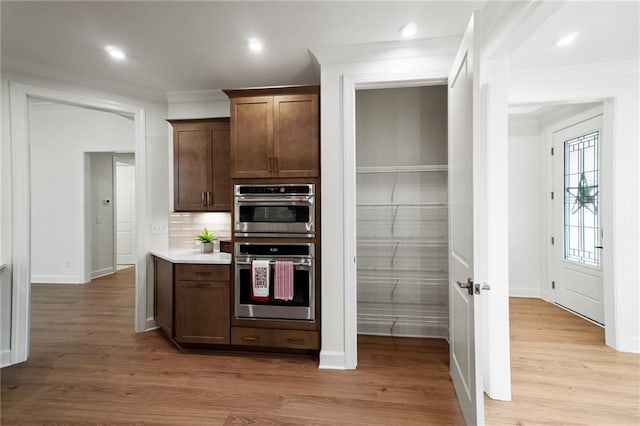 kitchen featuring stainless steel double oven, decorative backsplash, dark brown cabinets, and light hardwood / wood-style flooring