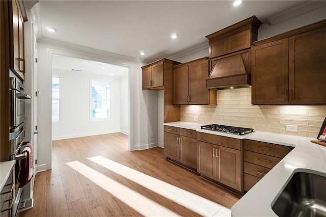 kitchen with premium range hood, stainless steel appliances, backsplash, light wood-type flooring, and crown molding