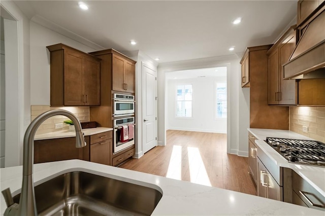 kitchen with premium range hood, decorative backsplash, sink, light hardwood / wood-style flooring, and light stone countertops