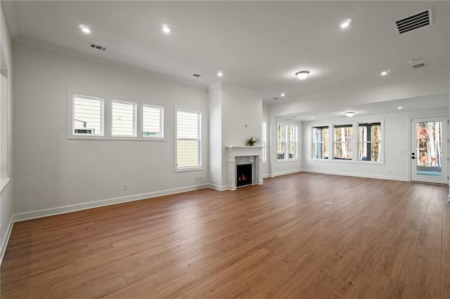 unfurnished living room featuring a wealth of natural light, wood-type flooring, and ornamental molding