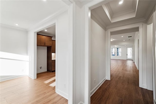 hallway featuring light wood-type flooring, crown molding, and a tray ceiling