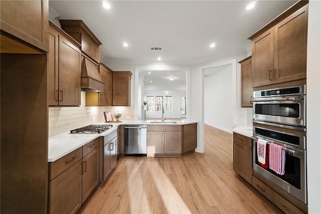 kitchen featuring premium range hood, stainless steel appliances, tasteful backsplash, light wood-type flooring, and sink