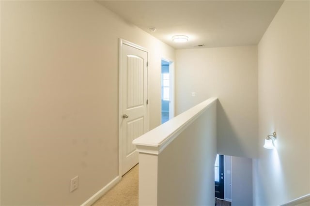 hallway featuring light colored carpet, baseboards, visible vents, and an upstairs landing