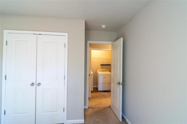 bedroom featuring washing machine and dryer, a closet, light colored carpet, and baseboards