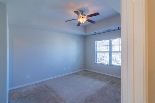 empty room featuring carpet floors, baseboards, a tray ceiling, and ceiling fan