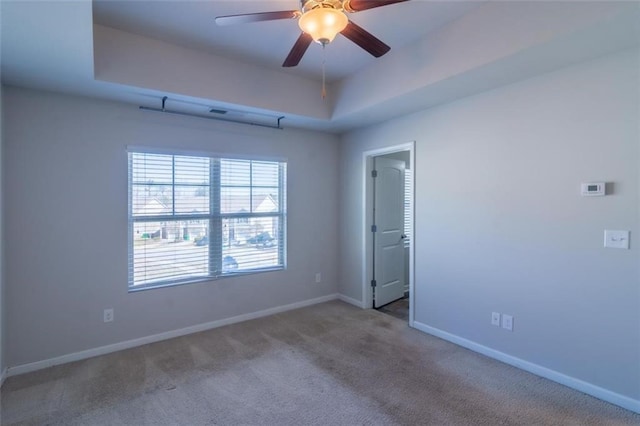 empty room featuring a tray ceiling, carpet, a ceiling fan, and baseboards