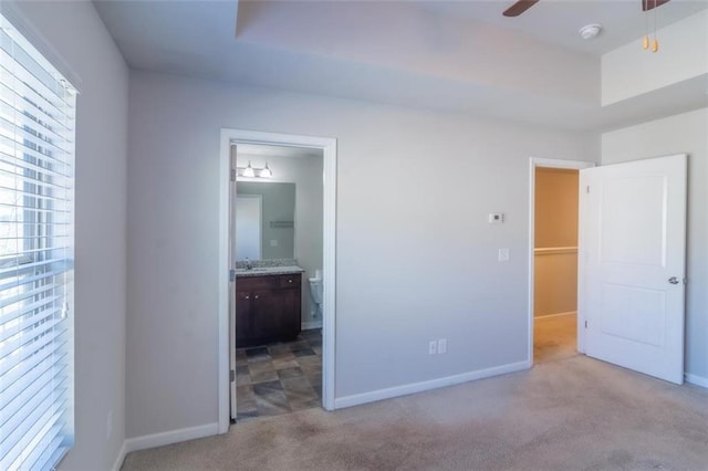 unfurnished bedroom featuring a raised ceiling, light colored carpet, a sink, ensuite bath, and baseboards