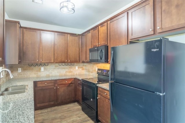 kitchen featuring decorative backsplash, a sink, black appliances, and light stone countertops