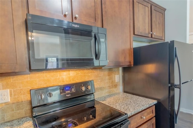 kitchen with black appliances, light stone counters, brown cabinetry, and decorative backsplash