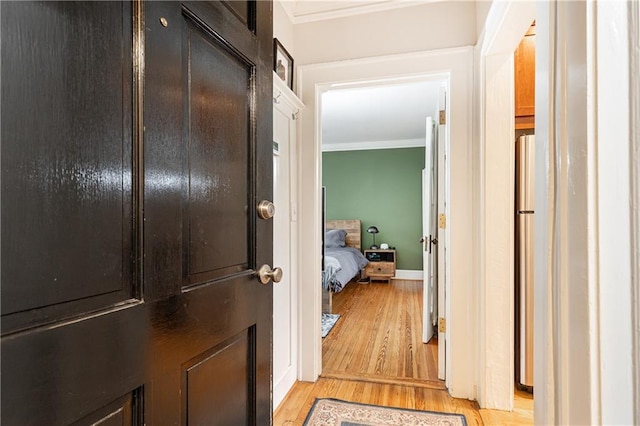 corridor featuring crown molding, light wood-type flooring, and baseboards