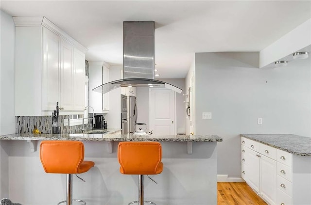 kitchen featuring island range hood, kitchen peninsula, light wood-type flooring, white cabinetry, and light stone counters