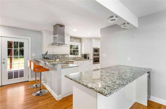 kitchen with white cabinetry, wall chimney range hood, light hardwood / wood-style floors, and kitchen peninsula