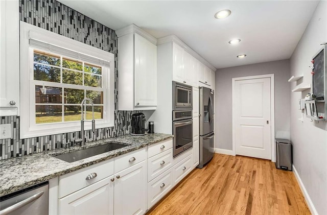 kitchen with light hardwood / wood-style flooring, stainless steel appliances, sink, light stone countertops, and white cabinets