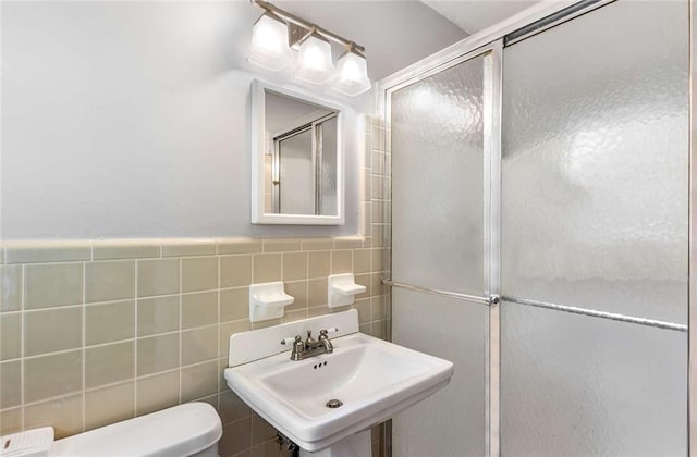 bathroom featuring toilet, tile walls, sink, and a shower with shower door