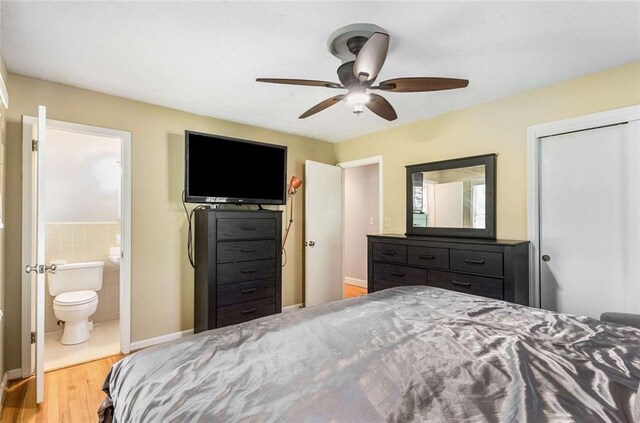 bedroom with connected bathroom, a closet, wood-type flooring, tile walls, and ceiling fan