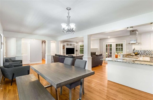 dining area featuring french doors, a notable chandelier, light wood-type flooring, and a brick fireplace