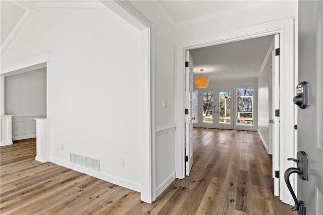 hall with light wood-type flooring, french doors, visible vents, and crown molding