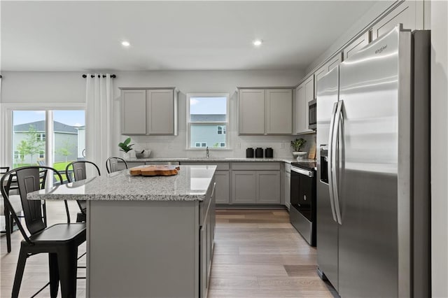 kitchen featuring backsplash, light stone countertops, a kitchen island, a kitchen bar, and stainless steel appliances