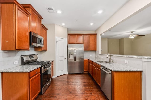 kitchen featuring stainless steel appliances, light stone counters, ceiling fan, and sink