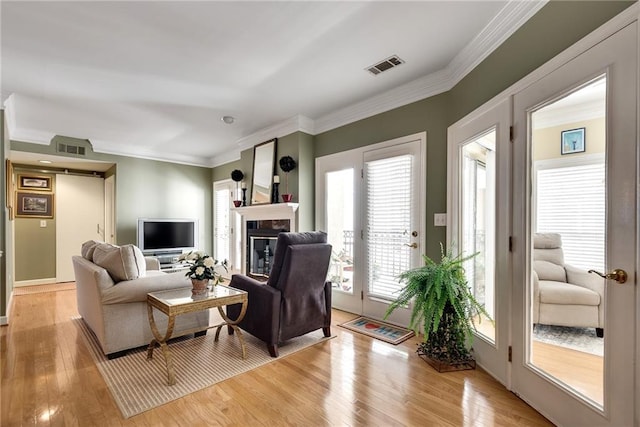 living area with a glass covered fireplace, crown molding, light wood-style floors, and visible vents