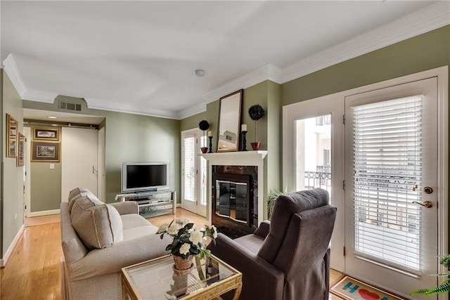 living room featuring crown molding, visible vents, baseboards, light wood finished floors, and a premium fireplace