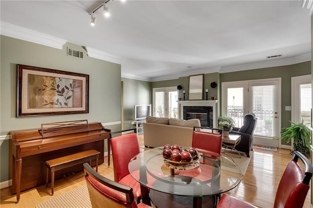 dining room featuring light wood-style floors, track lighting, a premium fireplace, and visible vents