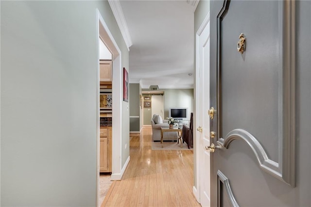 hallway featuring baseboards, ornamental molding, and light wood-style flooring