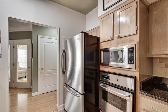 kitchen featuring appliances with stainless steel finishes, tasteful backsplash, light wood-type flooring, baseboards, and dark stone counters