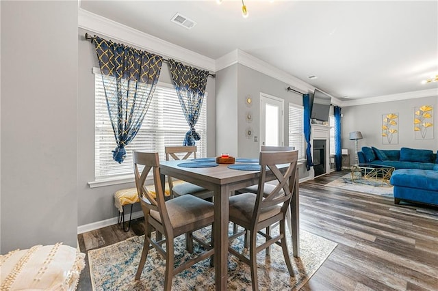 dining area featuring wood finished floors, visible vents, baseboards, ornamental molding, and a glass covered fireplace