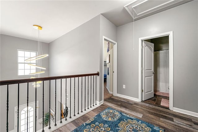 hallway featuring attic access, an inviting chandelier, baseboards, and wood finished floors