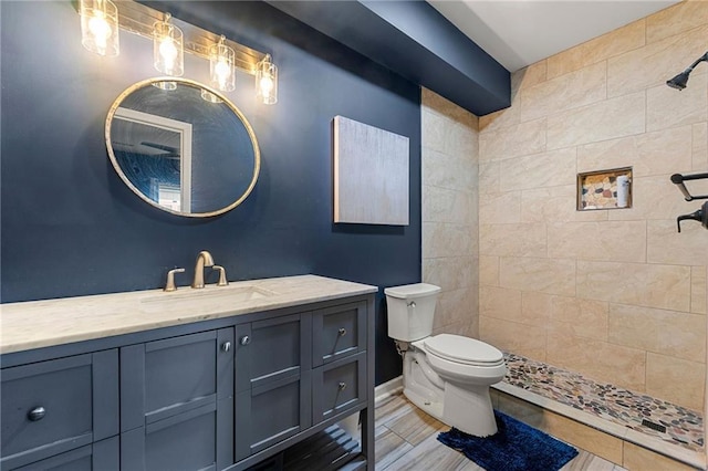 full bathroom featuring a tile shower, vanity, and toilet