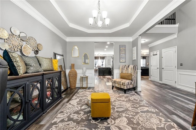 sitting room with crown molding, a raised ceiling, an inviting chandelier, wainscoting, and wood finished floors