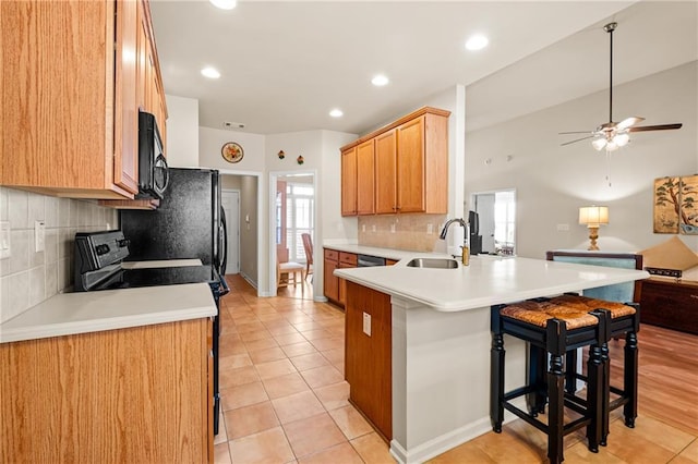 kitchen with a breakfast bar, a peninsula, a sink, black appliances, and open floor plan