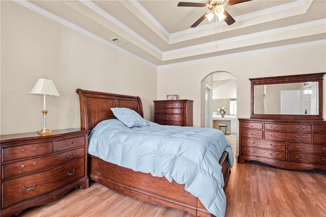 bedroom featuring visible vents, light wood-style flooring, ornamental molding, a tray ceiling, and ensuite bath