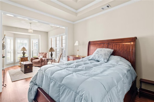 bedroom featuring baseboards, wood finished floors, visible vents, and ornamental molding